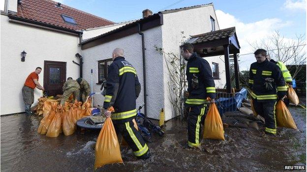 Firefighters and soldiers pile sandbags at the door of a home which is surrounded by flood water