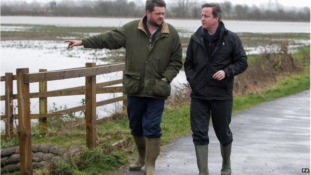 David Cameron speaks to farmer Tim Hook as they walk along a road next to flooded land