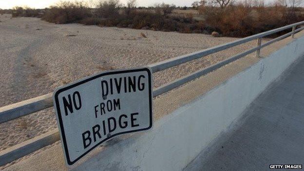 A "no diving" sign hangs on a bridge over the dry Kern River near Los Angeles, California.