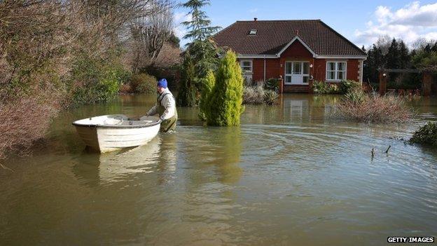 Danny Waller pushes a boat through his garden after his property flooded on February 16, 2014 in Chertsey