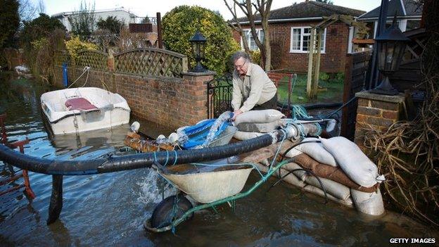 A man adjusts pipes that are removing flood water from his property in Chertsey