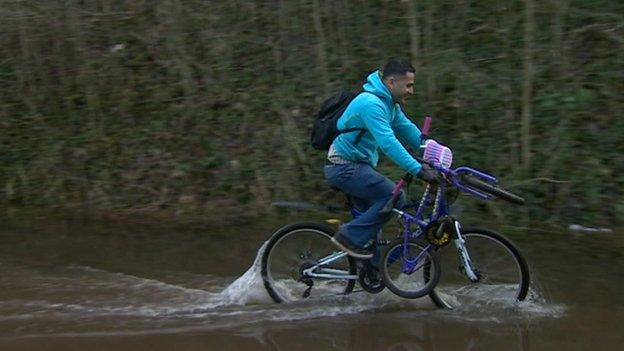 Man on bicycle on flooded cycle path