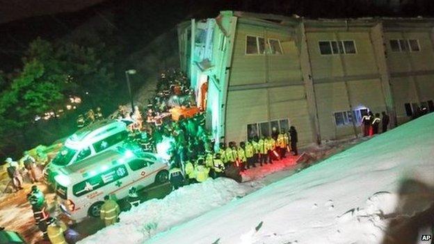 Partially collapsed auditorium building, surrounded by emergency workers