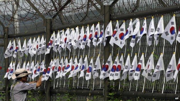 A South Korean man adjusts national flags on military wire fences at the Imjingak Pavilion near the border village of Panmunjom (August 2013)