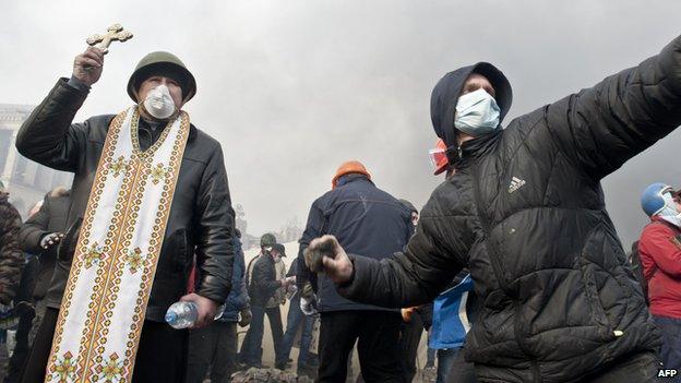 A protester throws rocks while another holds a cross