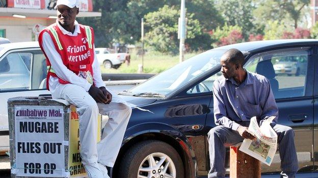 Men in Harare, Zimbabwe, near a poster with the headline: "Mugabe flies out for op" - February 2014