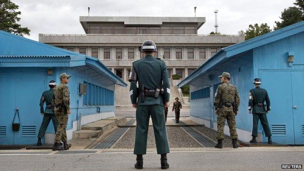 South Korean soldiers look towards the North Korean side as a North Korean solder approaches the UN truce village building that sits on the border of the Demilitarized Zone (DMZ), the military border separating the two Koreas