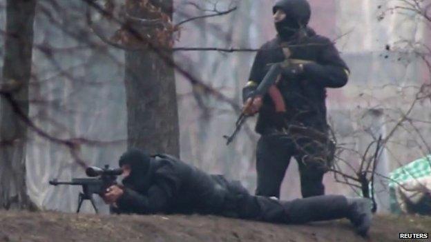 Video still provided by Radio Free Europe/Radio Liberty shows a riot police standing next to a sniper firing from a fortified position in the direction of protesters in Kiev (20 February 2014)