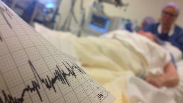 EEG trace in foreground with patient on bed and woman in scrubs in background