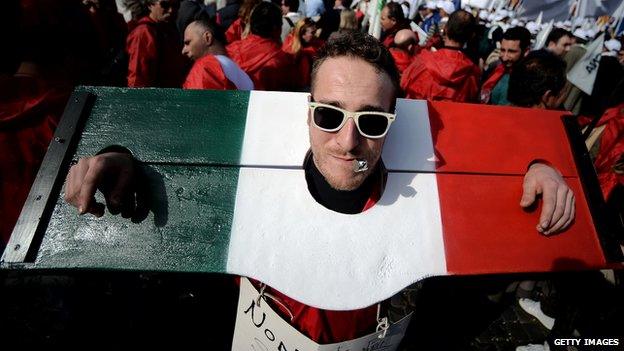 A protestor with his head and hands trapped in stocks in the colours of the Italian flag in a demonstration in Rome, 18 Feb 2014