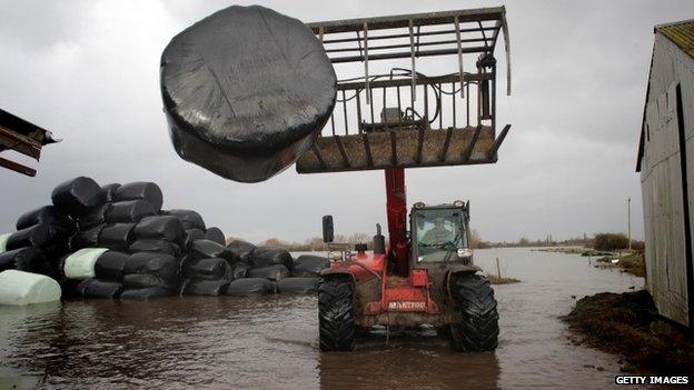 A farmer moves bales of animal feed at his flooded farm in Moorland, Somerset