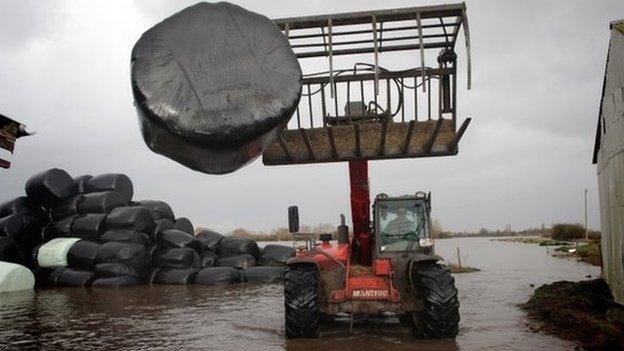 A farmer moves bales of animal feed at his flooded farm in Moorland, Somerset