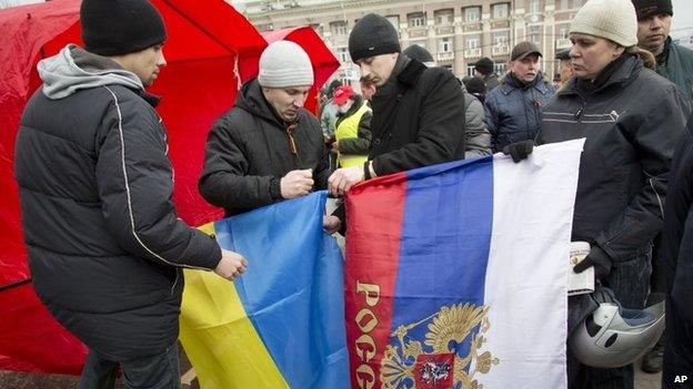 Pro-Russian activists tie together the Russian and Ukrainian flags as they gather below the statue of Vladimir Ilyich Lenin, in Donetsk,