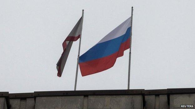 A Russian flag (R) is raised next to a Crimean flag on top of the Crimean parliament building in Simferopol