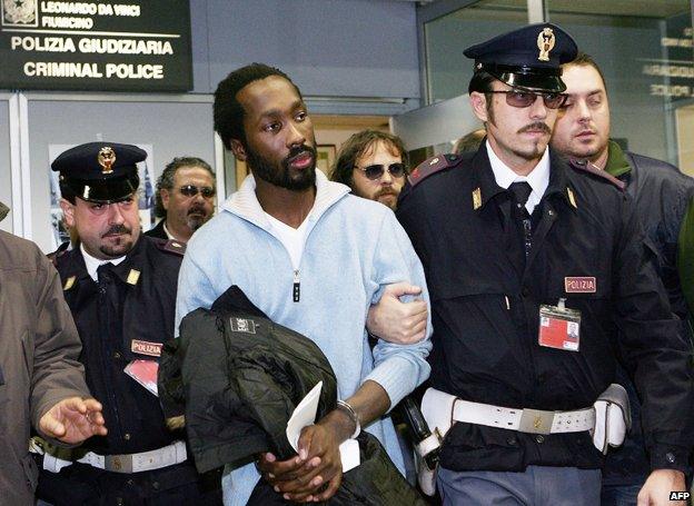 Rudy Hermann Guede (C), is escorted by police officers as he arrives at Rome's Fiumicino airport on 6 December 2007