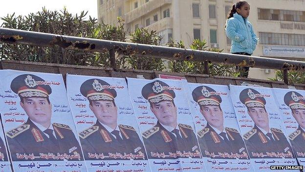 A girl stands above posters praising Abdel Fattah al-Sisi