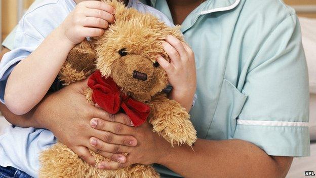 A teddy bear being cuddle by child and nurse