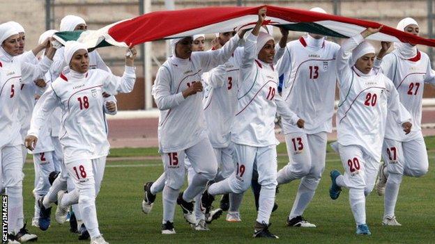 The Iranian women's football team run with their national flag