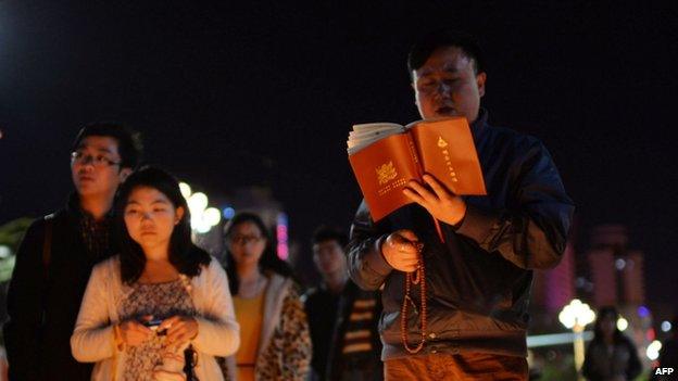 This picture taken on 2 March 2014 shows a Buddhist (R) chanting prayers as mourners light candles at the scene of the terror attack at the main train station in Kunming, southwest China's Yunnan province