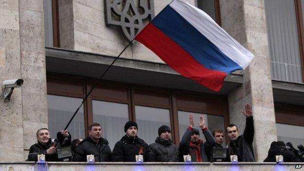 Demonstrators holding a Russian flag, with the Ukrainian emblem in the background, stand on the balcony of the regional administrative building after storming it in Donetsk