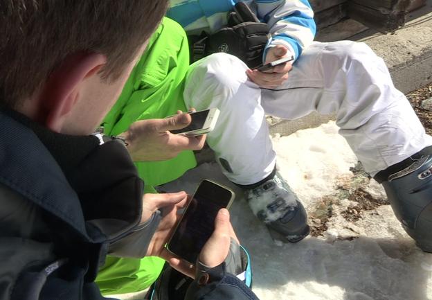 Three men in ski boots look at smartphones