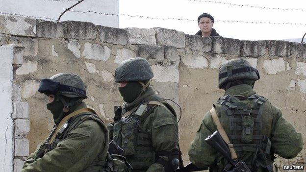 A Ukrainian serviceman (rear) looks at uniformed men, believed to be Russian servicemen, standing guard at a Ukrainian military base in a village outside Simferopol, Crimea, 6 March 2014