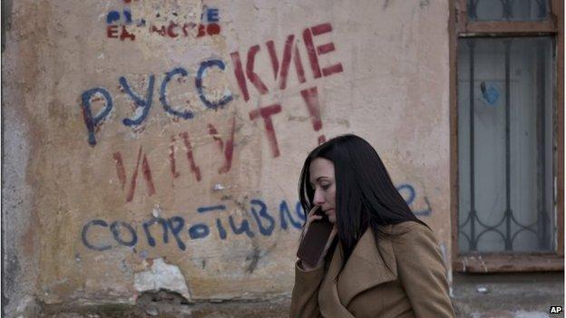 A woman passes by graffiti that reading "The Russians are coming - Resistance" in Simferopol, Crimea