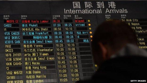 A man stands beside the arrival board at Beijing airport, which shows the missing flight MH370