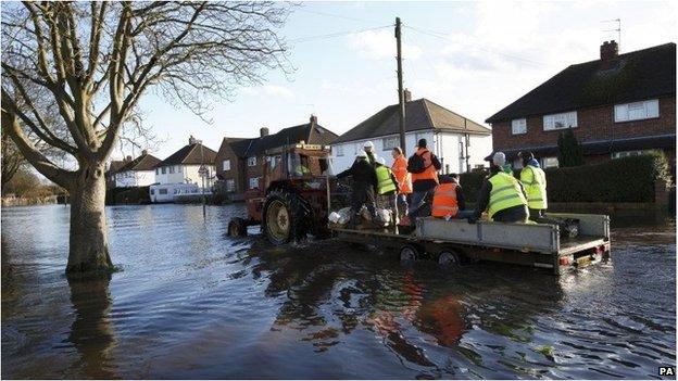 Tractor and trailer pass through flooded street in Egham