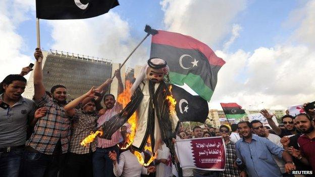 Protesters burn an effigy of Qatar's emir as they wave the flags of Cyrenaica and Libya during a rally against the Muslim Brotherhood and Qatar in Benghazi (10 May 2013)