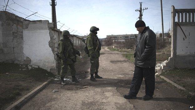 A member of a pro Russian self-defence unit (right) stands close to Russian Army soldiers outside the Ukrainian army base in Perevalnoe, Crimea