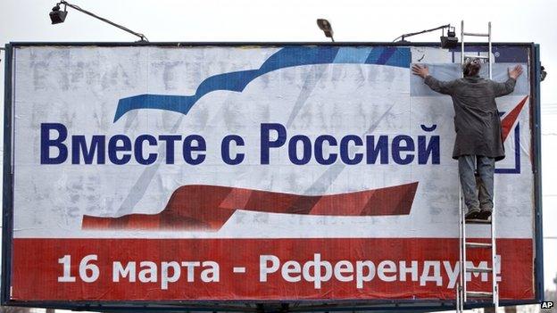 A man pastes a poster advertising the referendum in Crimea that reads "Together with Russia! March 16 - Referendum!" in Simferopol, Ukraine