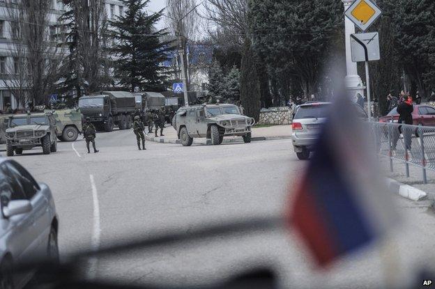 Troops in unmarked uniforms stand guard in Balaklava as people walk in a street, on the outskirts of Sevastopol, Ukraine, Saturday, March 1, 2014.