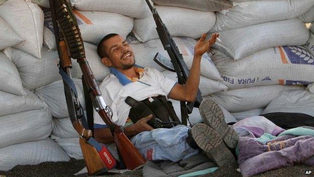 Flanked by weapons a vigilante leans against a barricade at the entrance of Apatzingan on 9 February, 2014