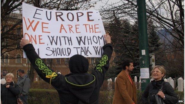 A protester holding a sign reading "Europe: We are the one with whom U should talk"