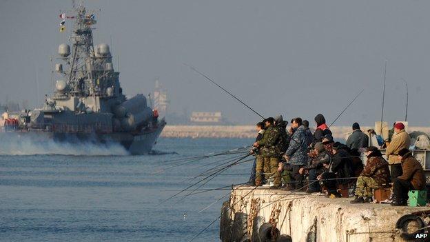 People fish as a Russian naval vessel passes by in Sevastopol bay, Crimea, on 12 March 2014