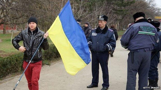 Police officers stand by as a pro-Ukrainian supporter holding a Ukrainian flag parades in Simferopol