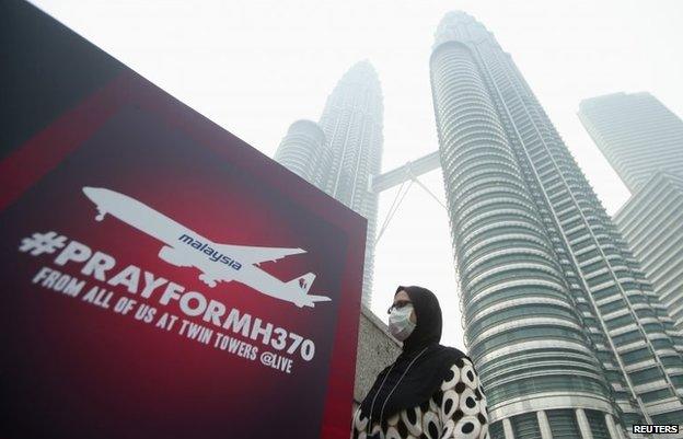 A woman wearing a mask against the haze walks past a board saying "Pray for MH370" in Kuala Lumpur, March 14