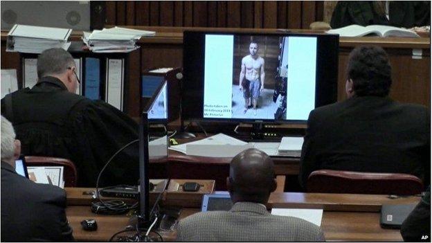 An image taken from the court pool TV via AP showing on screen a police photograph of Oscar Pistorius standing on his blood-stained prosthetic legs and wearing shorts covered in blood, taken shortly after the athlete fatally shot his girlfriend, which was shown to the court in Pretoria, at his murder trial Friday, March 14, 2014.