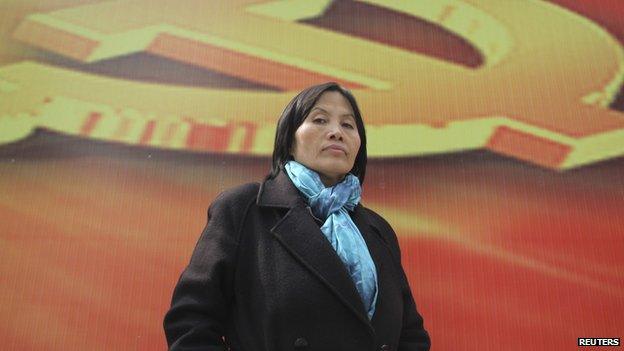 Prominent Chinese human rights activist Cao Shunli stands in front of an emblem of the Chinese Communist Party during an interview in the central business district of Beijing March 23, 2013