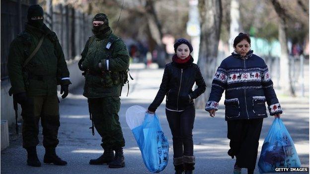 Members of the public walk past pro-Russian troops in Simferopol, Crimea (17 March 2014)