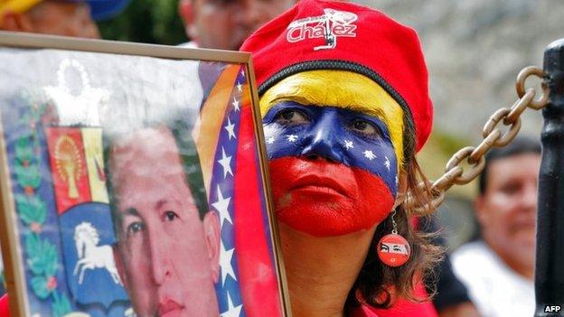 Handout photo released by the Venezuelan Presidency of a supporter of Venezuelan President Nicolas Maduro holding a portrait of late Venezuelan President Hugo Chavez during a rally at the presidential palace in Caracas on 16 March, 2014