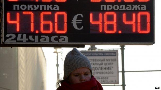 A woman stands under a board listing foreign currency rates against the Russian ruble just outside an exchange office in central Moscow (January 2014)