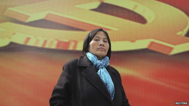 Prominent Chinese human rights activist Cao Shunli stands in front of an emblem of the Chinese Communist Party during an interview in the central business district of Beijing 23 March 2013