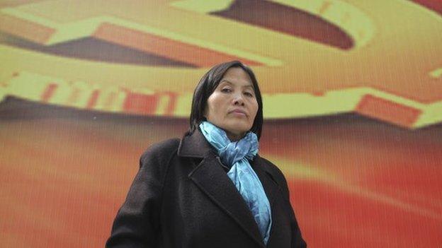 Prominent Chinese human rights activist Cao Shunli stands in front of an emblem of the Chinese Communist Party during an interview in the central business district of Beijing 23 March 2013