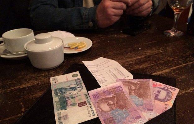 A 1,000-rouble note lies side by side with 300 Ukrainian hryvnya on a restaurant table in Yalta, Crimea. The sums are roughly equivalent