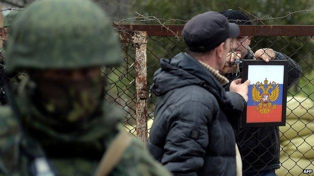 The Russian coat of arms is placed on the gate as Russian soldiers stand guard after they took control of the Ukrainian navy south headquarters base in Novoozerne on March 19, 2014.