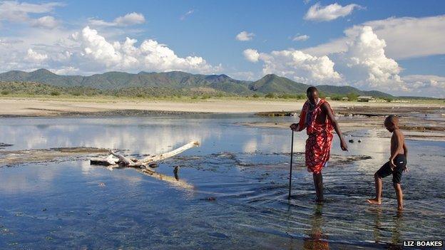 A man helps a younger boy cross a lake