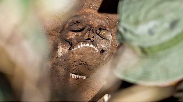 A coroner examines a body in the site of a unmarked grave