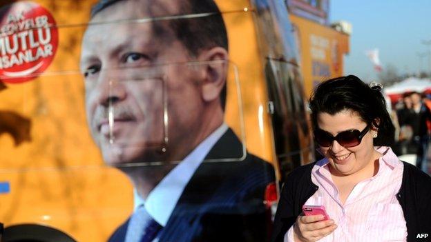 Woman uses her smartphone as she walks past a portrait of Turkish PM Recep Tayyip Erdogan (21 March 2014)